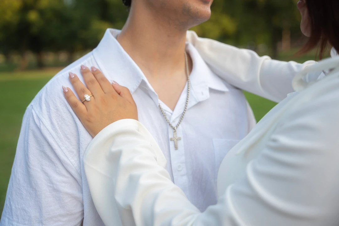 A close view of an engagement ring and white shirts during an embrace.