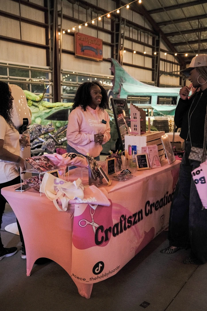 Visitors and makers at a pink-covered holiday market table.