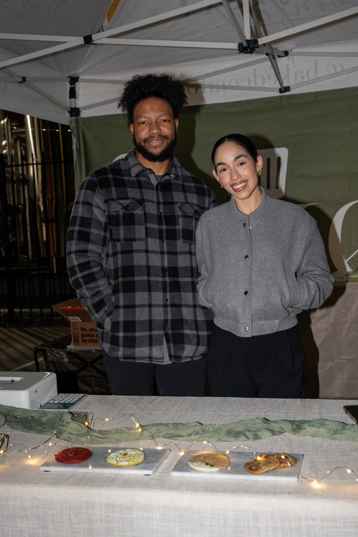 Two makers behind a table of individually wrapped baked goods.