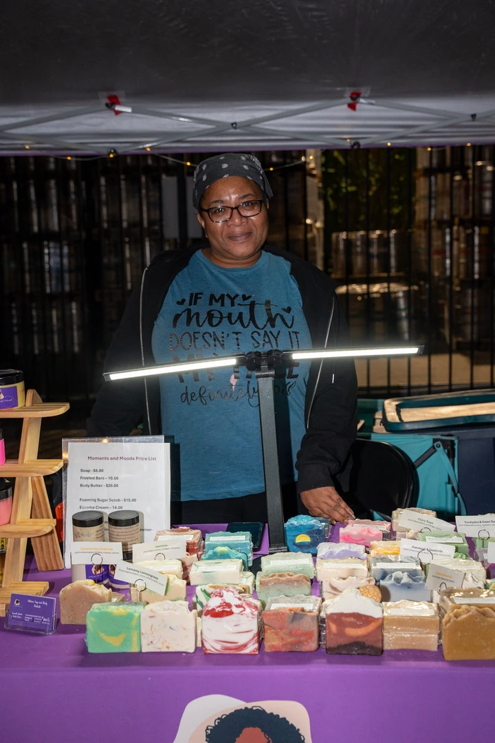 A maker behind a brightly lit soap and gift display.