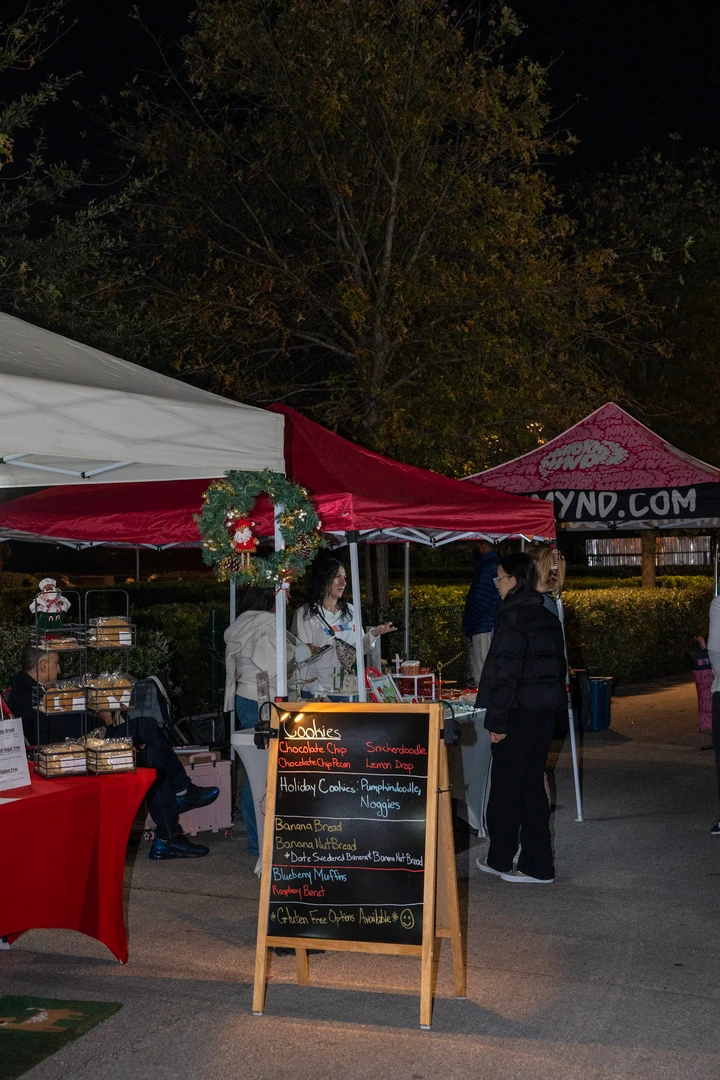 Shoppers walking between outdoor market tents after dark.