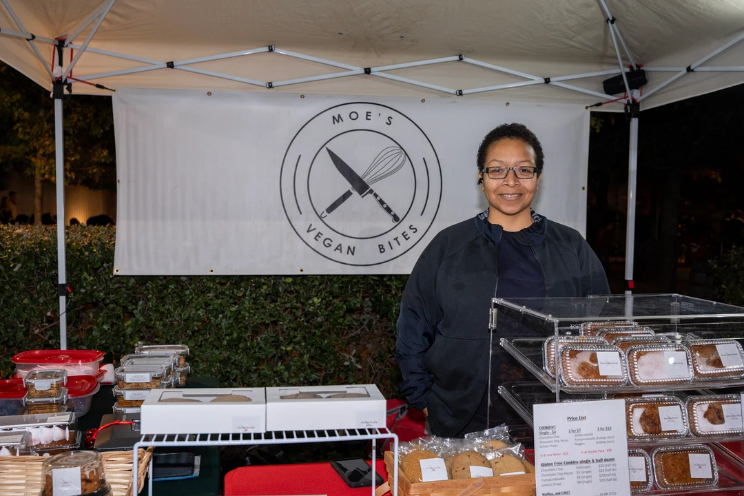 A smiling baker behind a table of packaged baked goods.