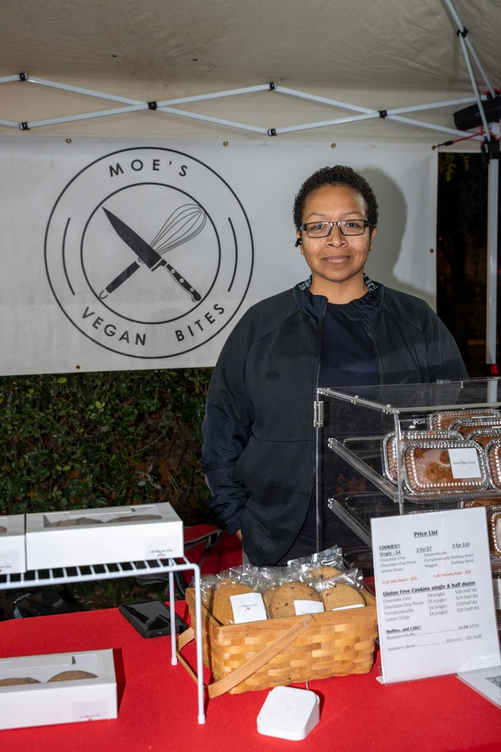 A smiling baker behind a table of packaged baked goods.