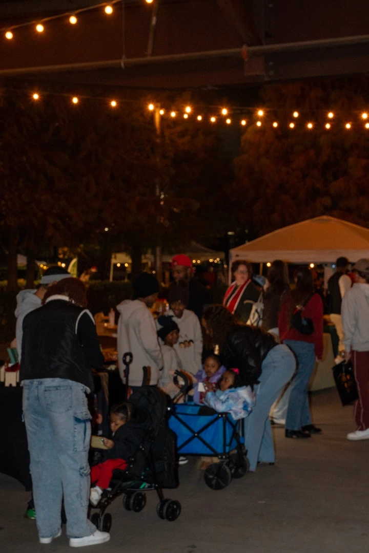 Market visitors gathering outdoors beneath string lights.
