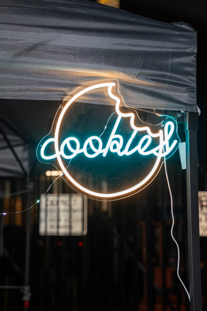 A glowing circular Cookies sign beneath a night-market canopy.