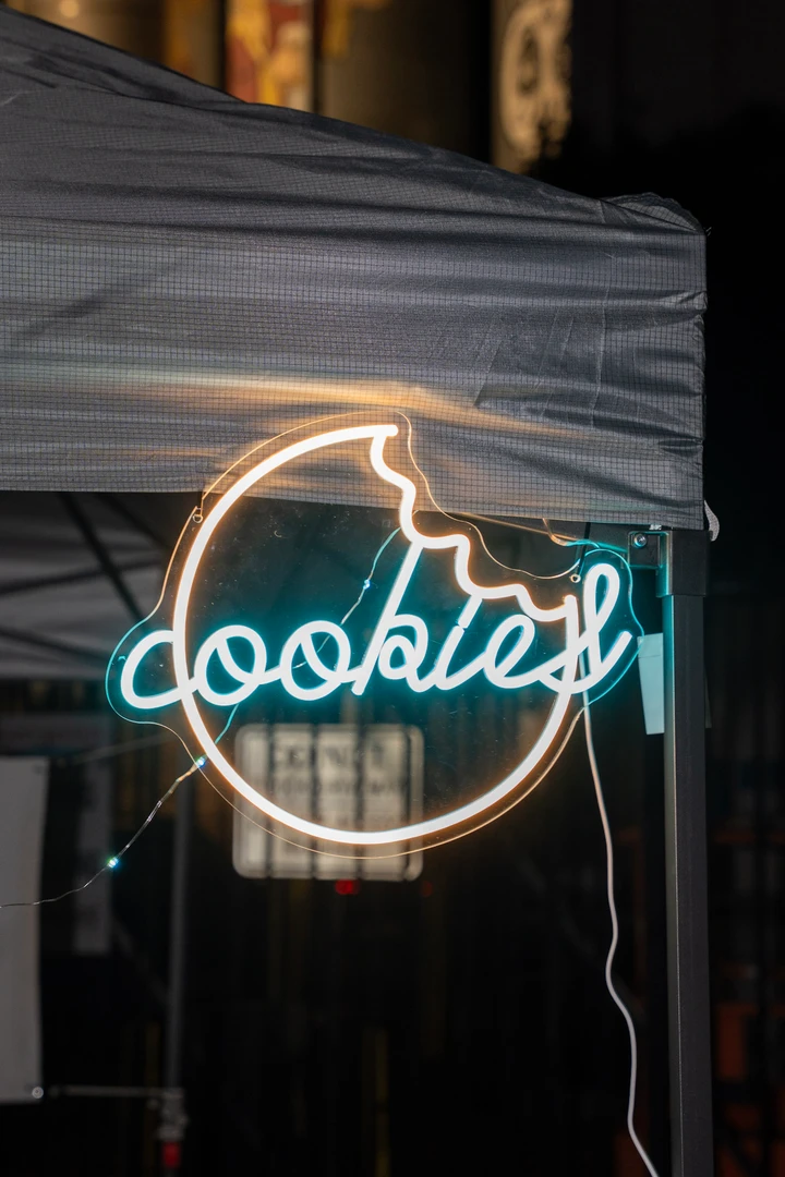 A glowing circular Cookies sign beneath a night-market canopy.