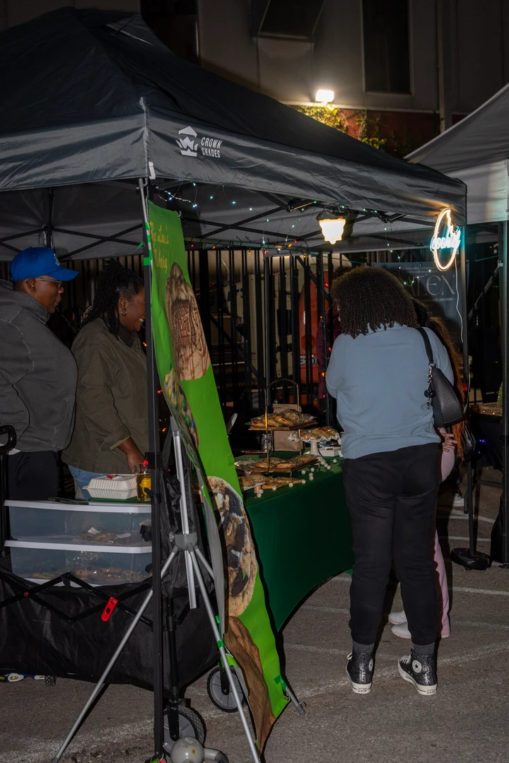 Shoppers browsing a cookie stall beneath evening lights.