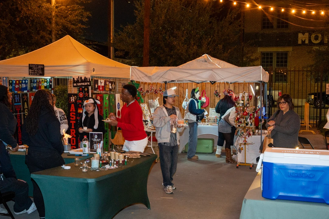 Shoppers browse outdoor market stalls beneath evening string lights.