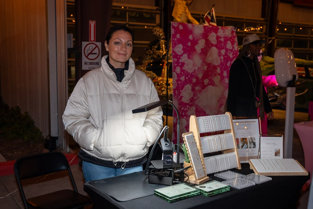 A smiling maker in white behind her jewelry display.