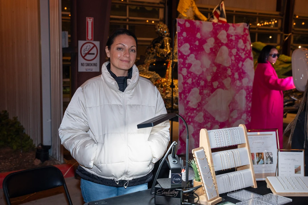 A smiling maker in white behind her jewelry display.