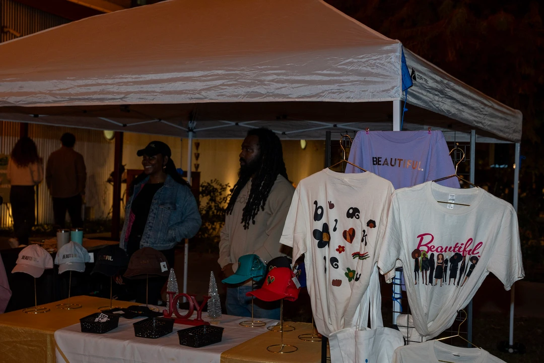 Vendors behind a display of printed shirts beneath a white canopy.