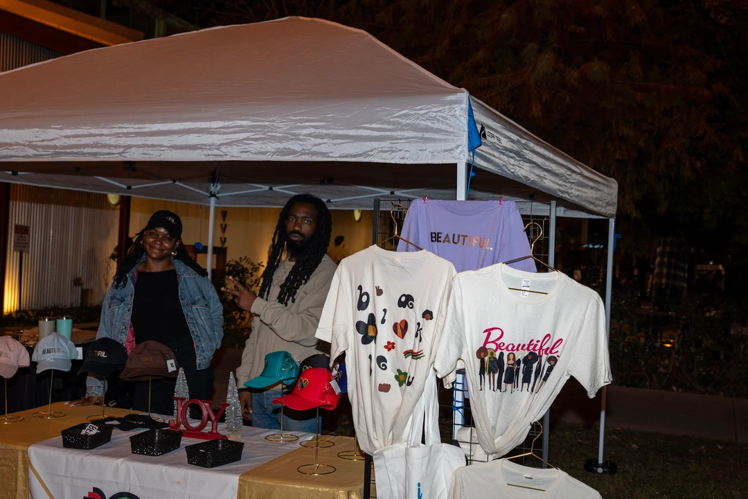 Vendors behind a display of printed shirts beneath a white canopy.