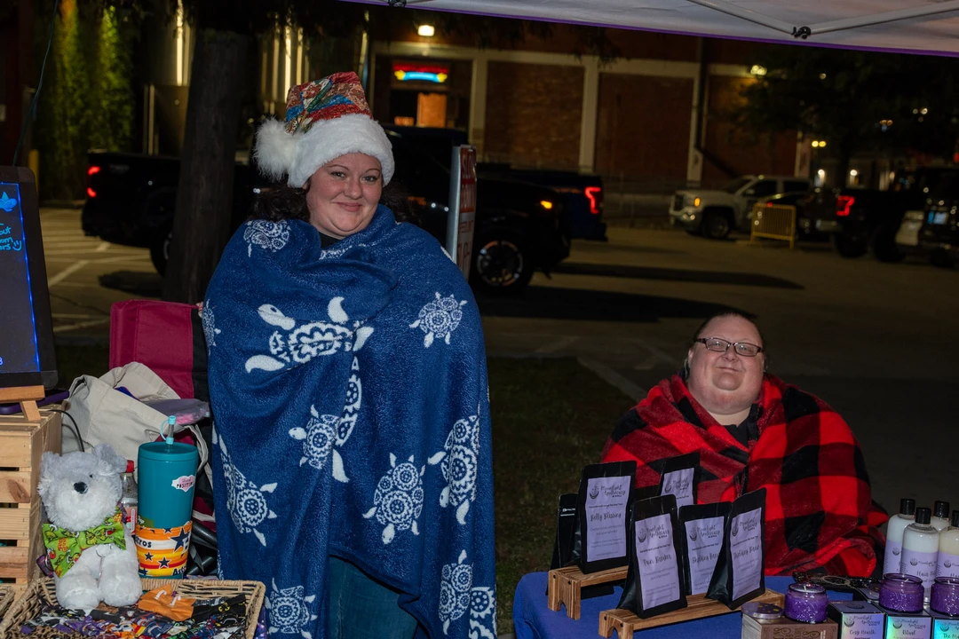 Two festive vendors beside their holiday market table.