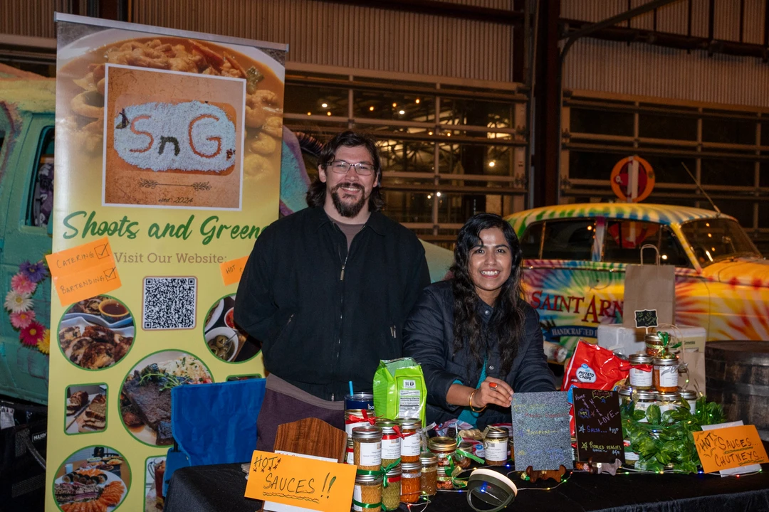 Two vendors behind a sauce and seasoning display.