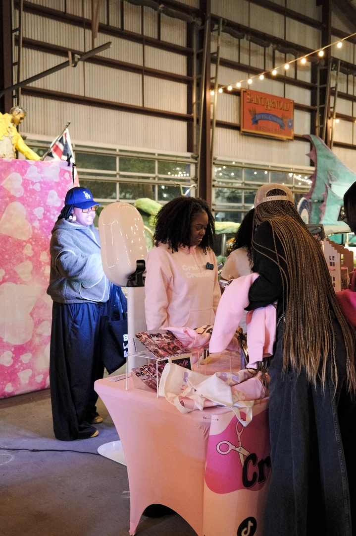 Visitors and makers at a pink-covered holiday market table.