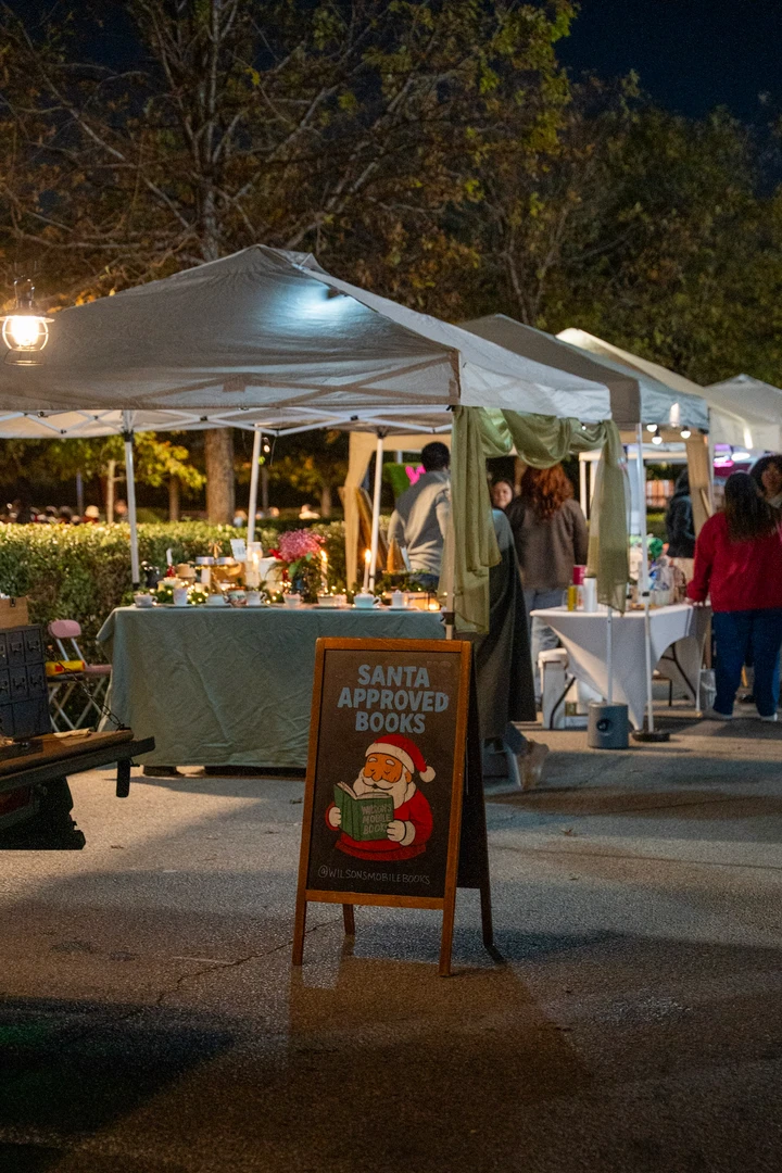 Outdoor market tents and a bookshop menu board at night.