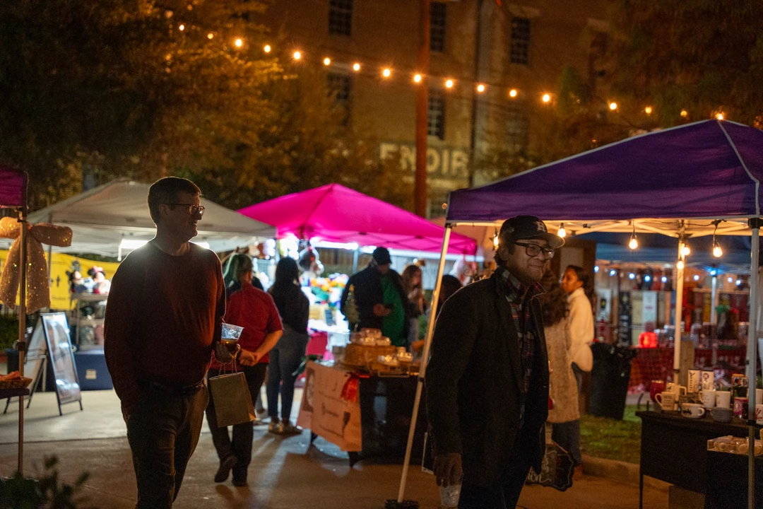 Visitors walking past market tents beneath warm string lights.