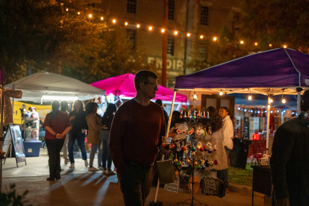 Visitors walking past market tents beneath warm string lights.
