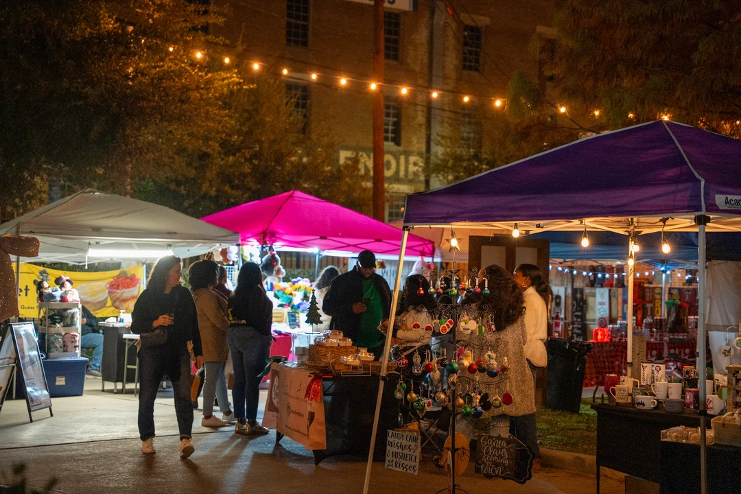 Visitors walking past market tents beneath warm string lights.
