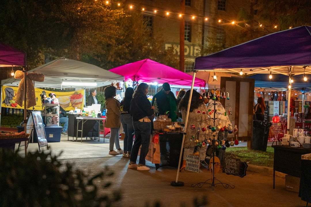 Visitors walking past market tents beneath warm string lights.