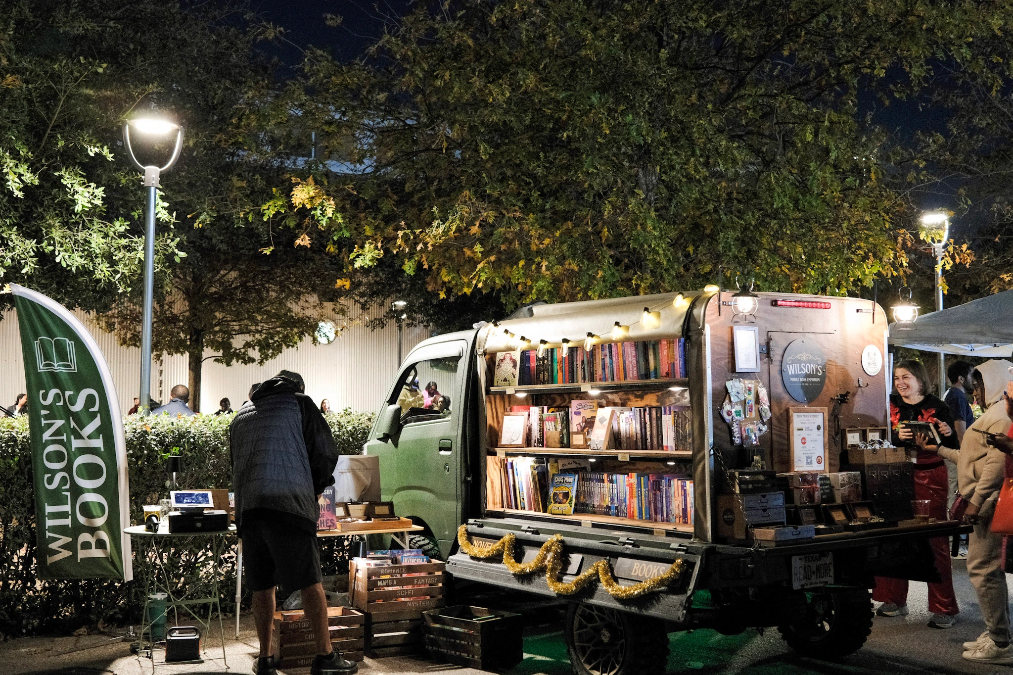 A small mobile bookshop sits beside the night market with its shelves lit up.