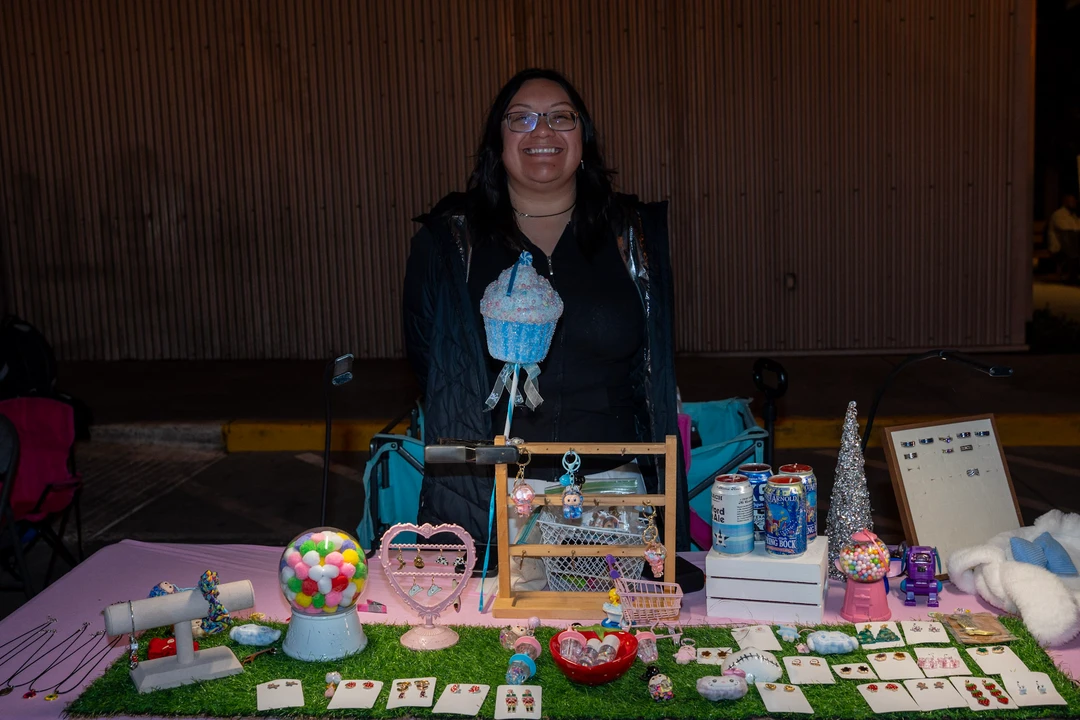 A smiling maker behind a table of jewelry and accessories.
