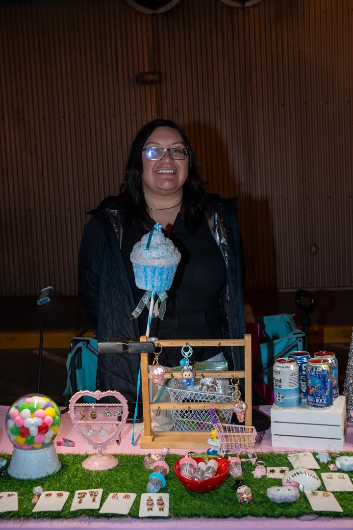 A smiling maker behind a table of jewelry and accessories.