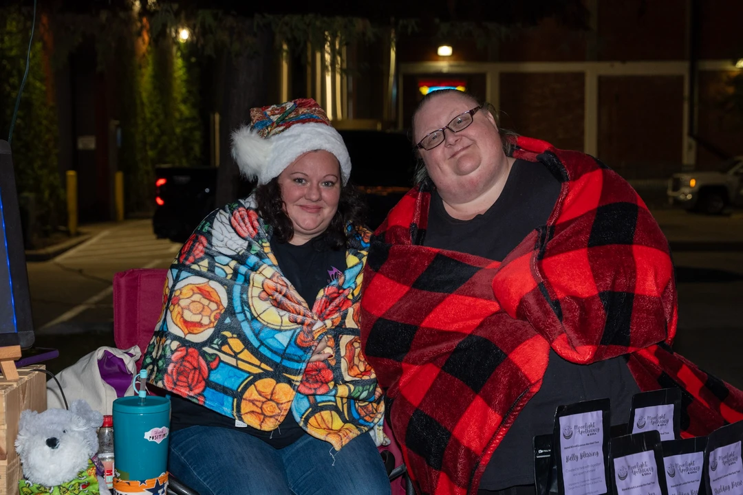 Two smiling vendors seated beside their holiday display.