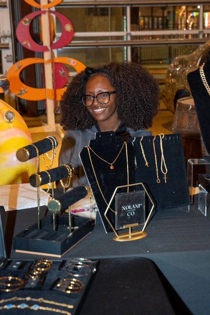 A smiling jewelry maker behind a dark display table.