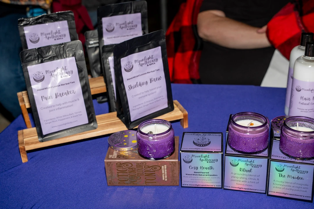 Handmade soap and small packaged goods on a purple tablecloth.