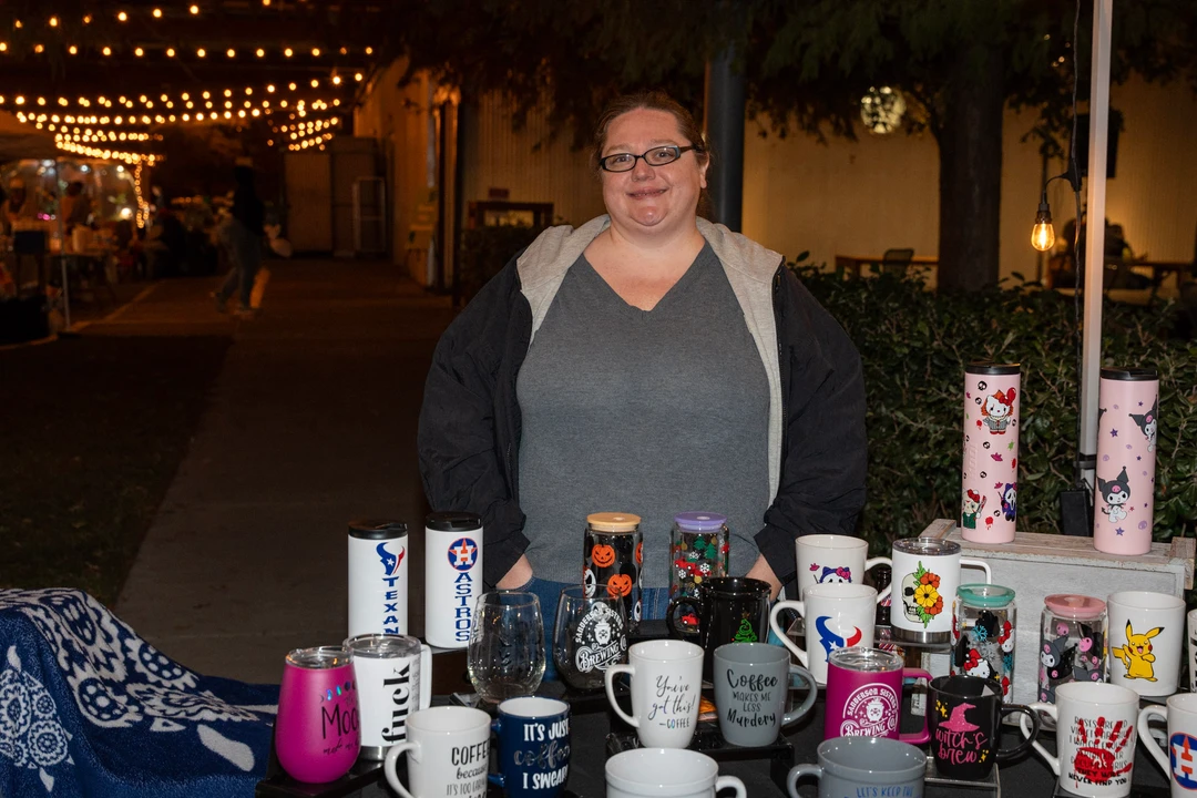 A maker with short hair behind a table of candles and gifts.