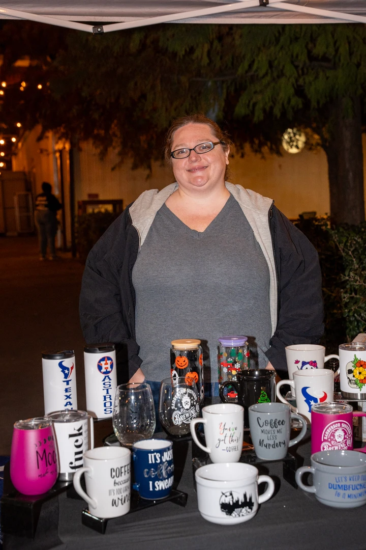 A maker with short hair behind a table of candles and gifts.