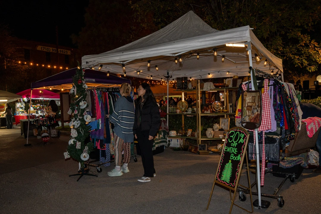 Visitors browsing illuminated outdoor stalls beneath white tents.