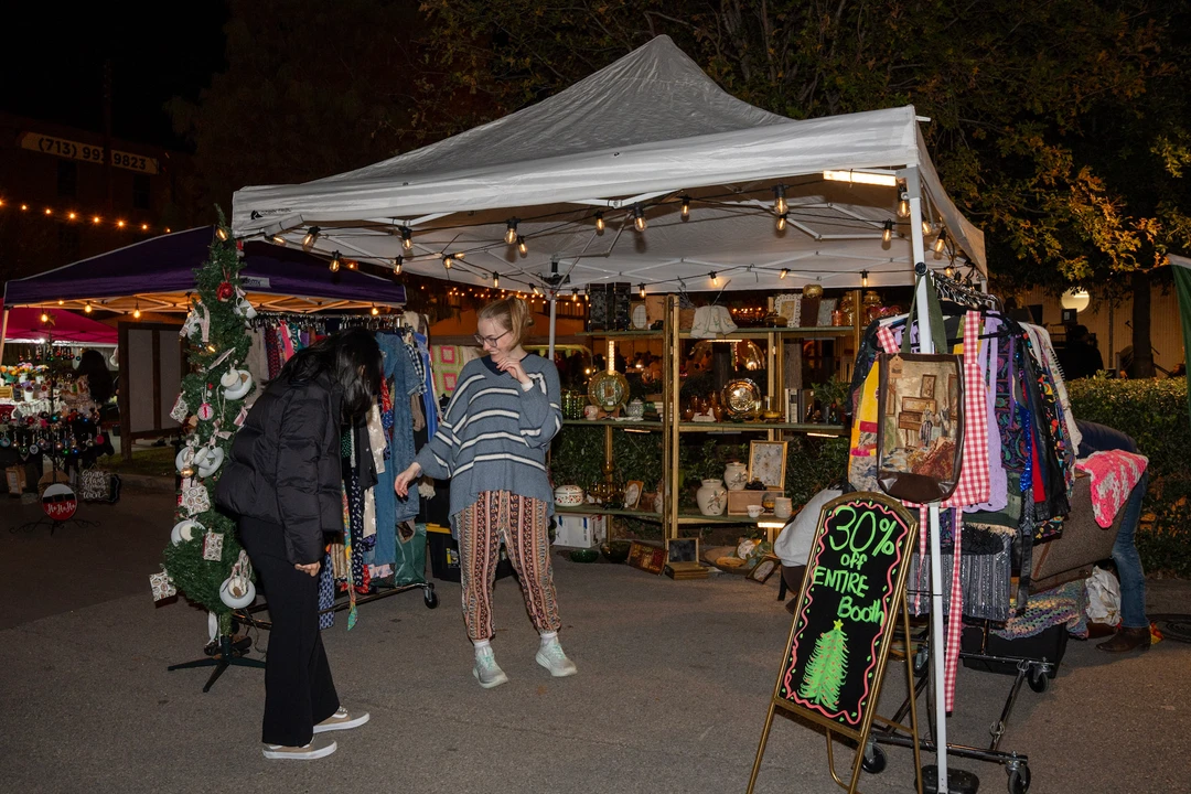 Visitors browsing illuminated outdoor stalls beneath white tents.