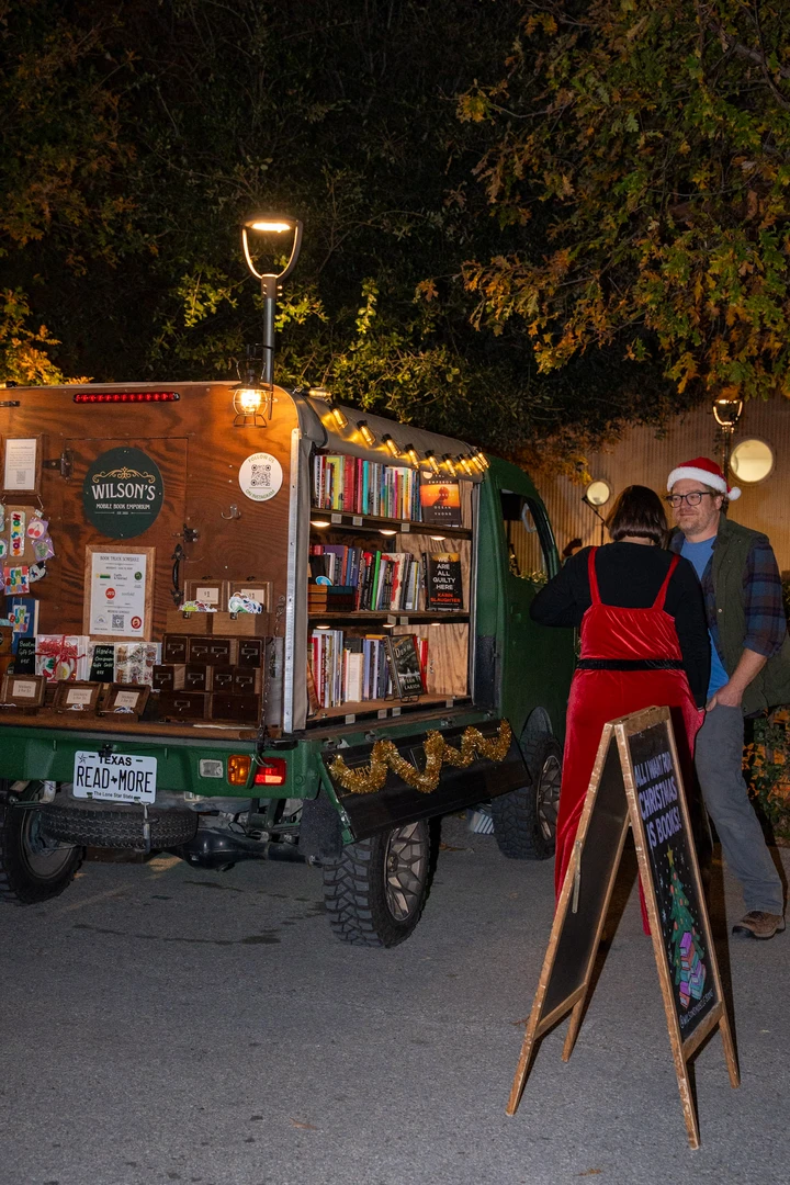 Visitors and shelves of books at the illuminated mobile bookshop.