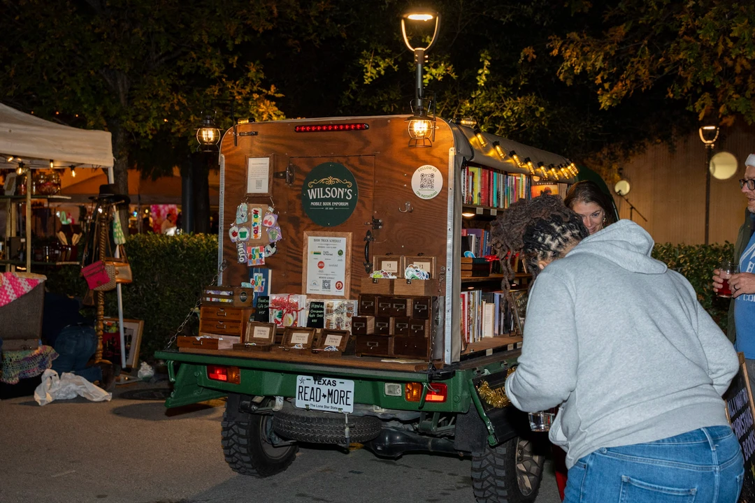 Visitors and shelves of books at the illuminated mobile bookshop.