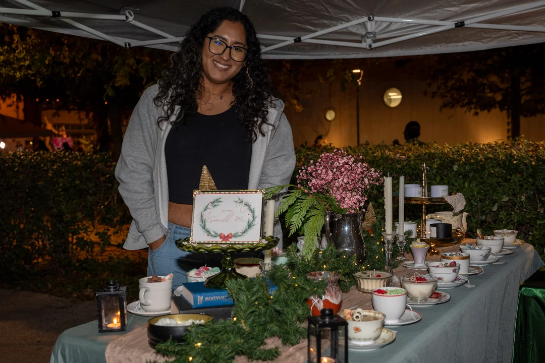 A floral maker smiles behind her display of flowers and greenery.