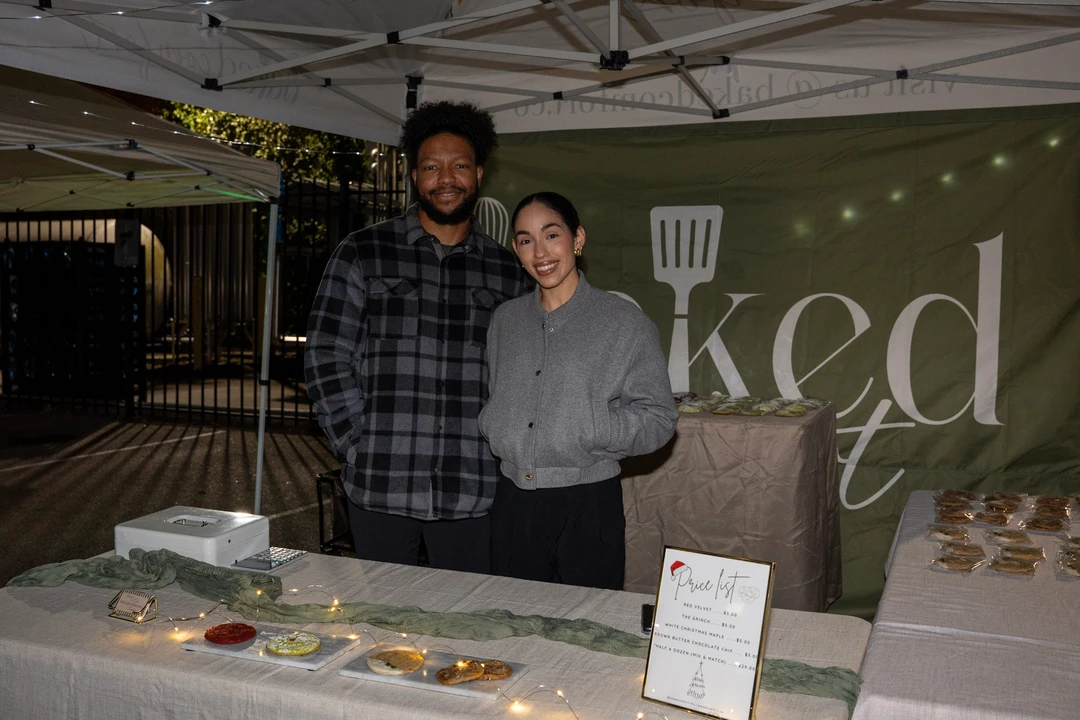 Two makers behind a table of individually wrapped baked goods.