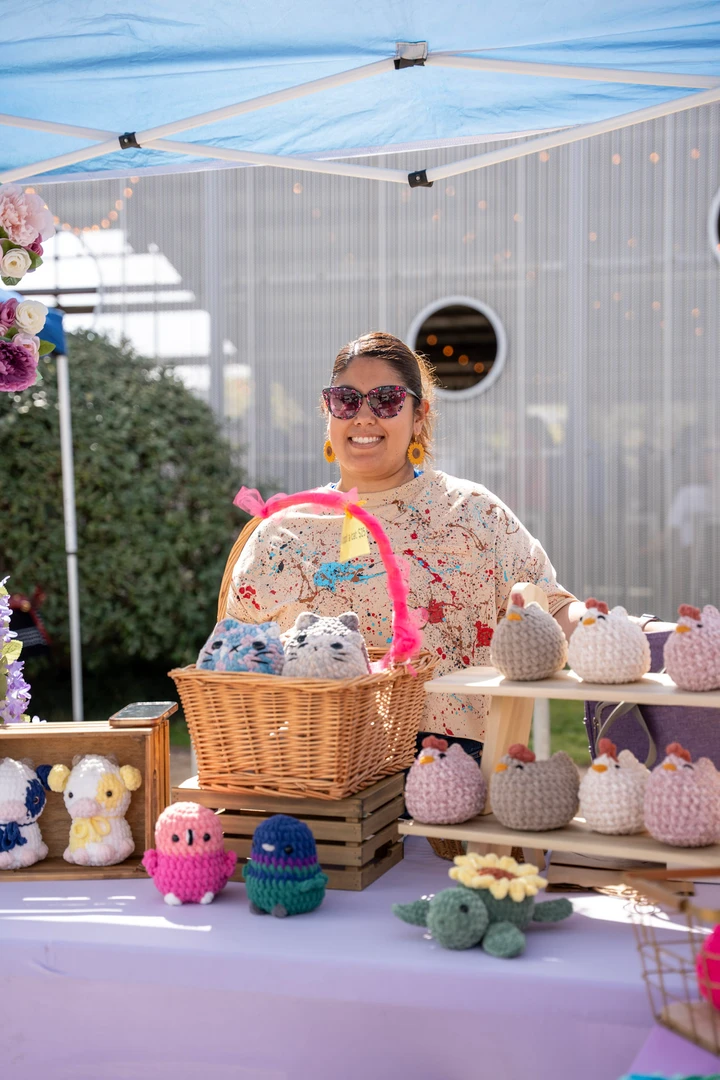A maker behind a table of colorful crocheted toys.