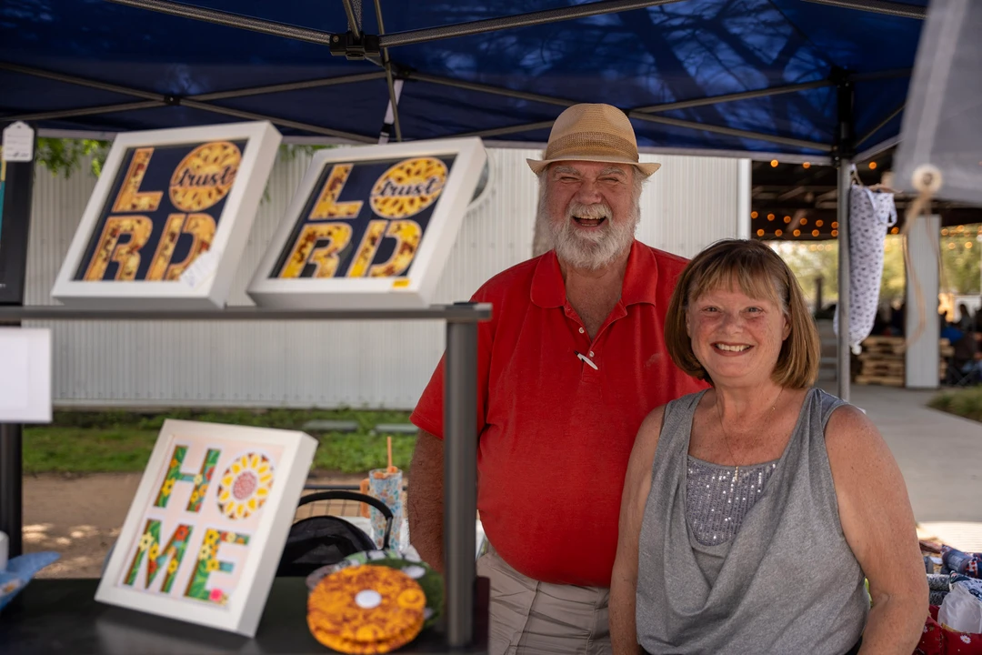 Two makers standing behind a table of crafts and framed pieces.