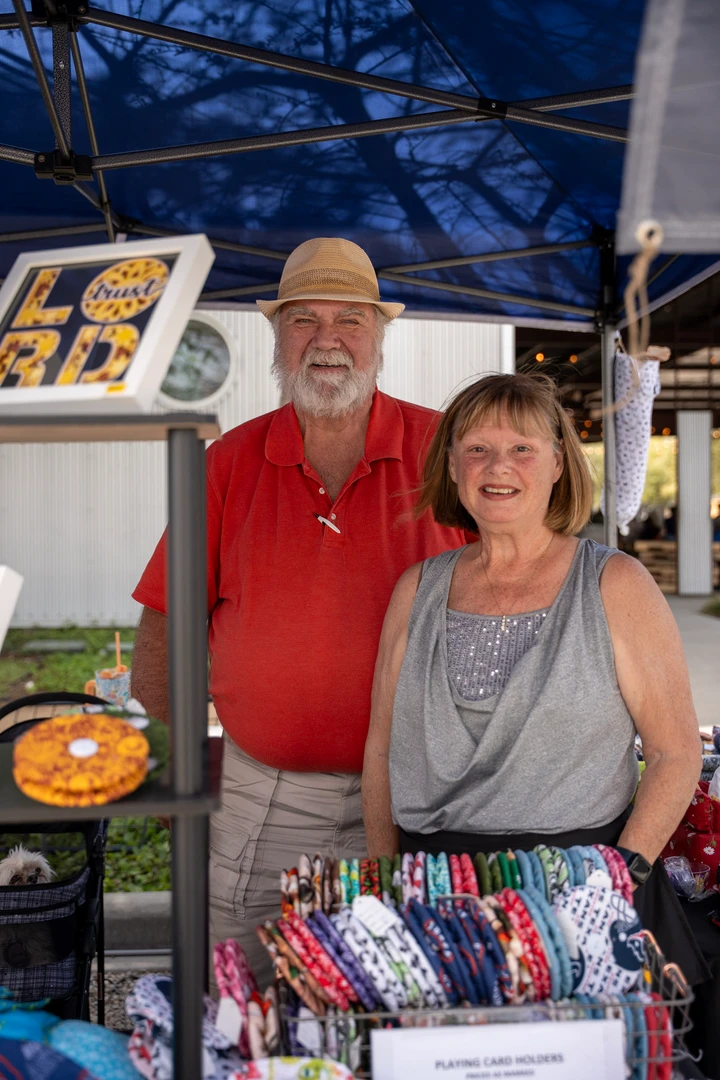 Two makers standing behind a table of crafts and framed pieces.