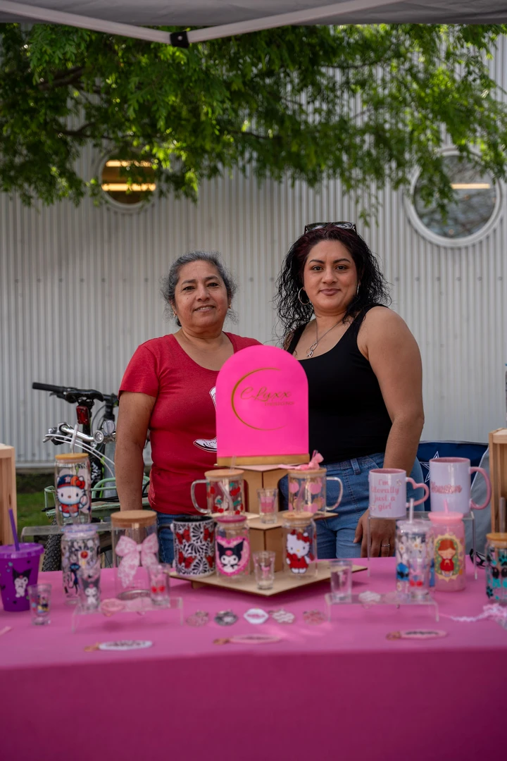 Two makers behind a bright pink jewelry display.