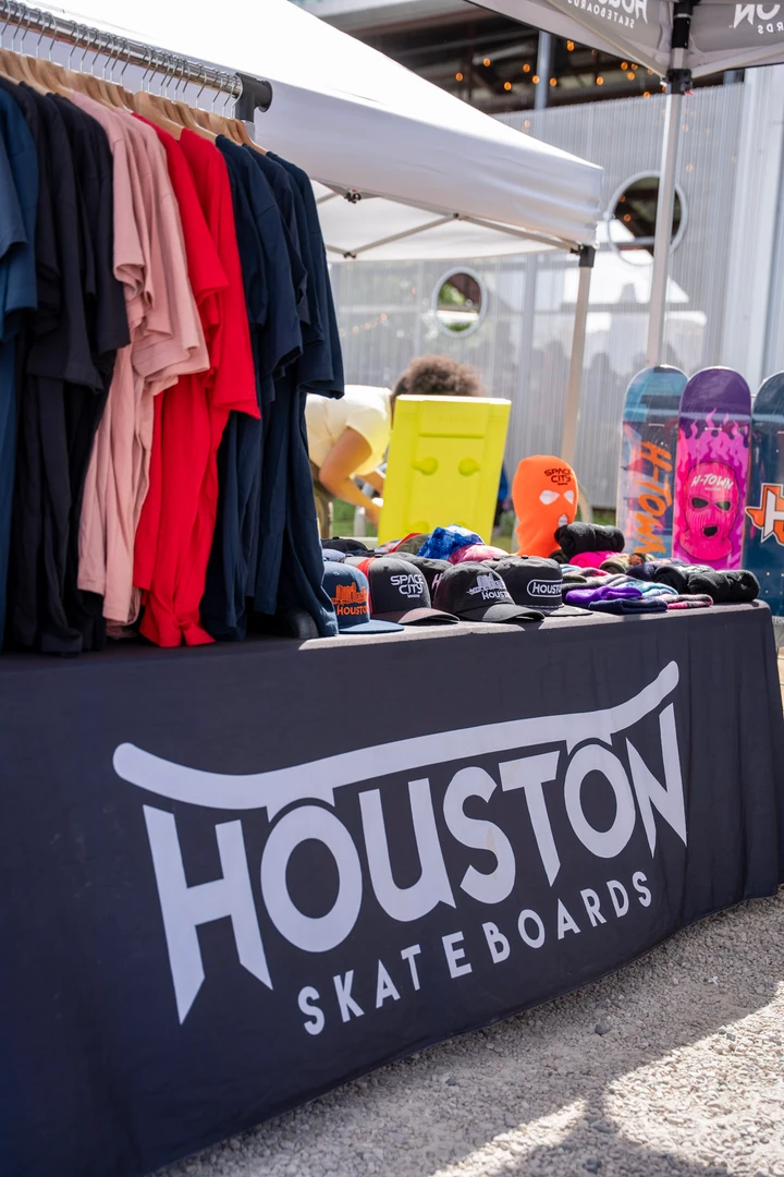 A Houston Skateboards table beside a clothing rack.