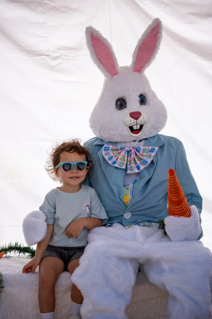 A child sitting beside a person dressed as a rabbit.