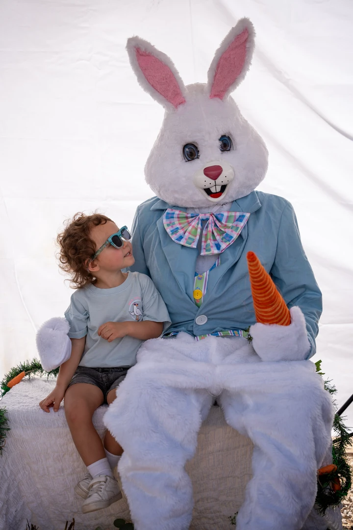 A child sitting beside a person dressed as a rabbit.