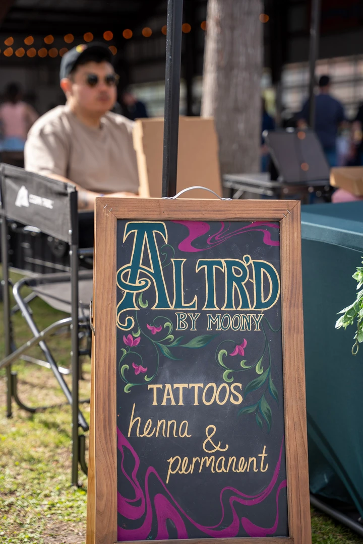 A vendor behind a temporary tattoo sign.