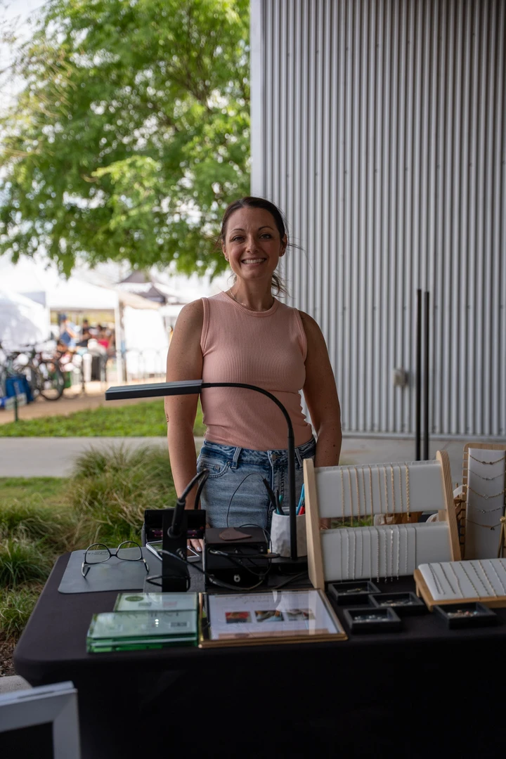 A maker standing behind a jewelry table.