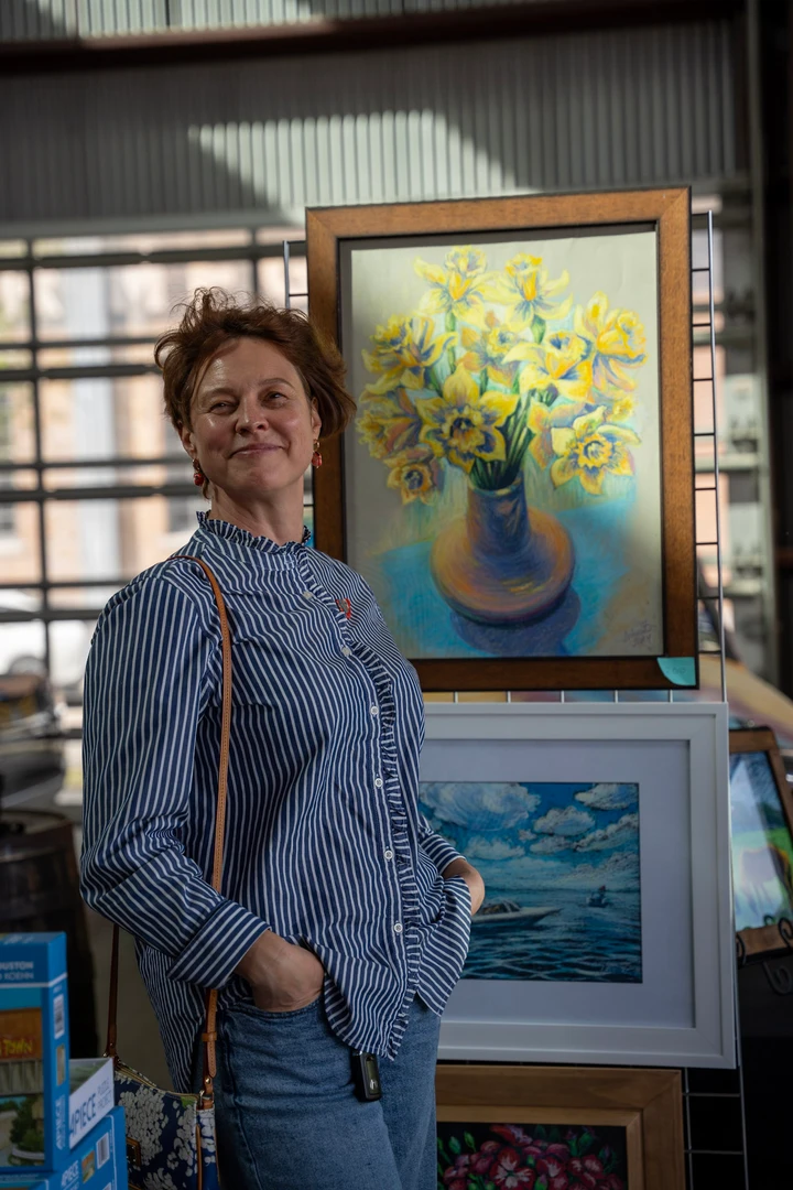 An artist standing beside framed paintings.