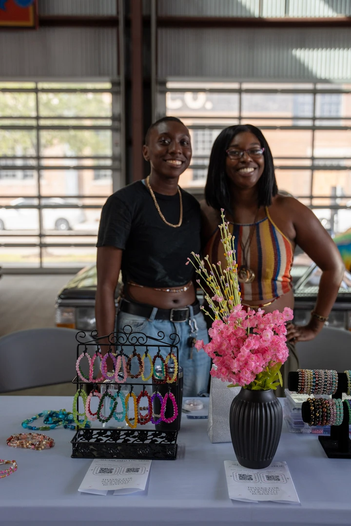 Two vendors behind a colorful accessories table.