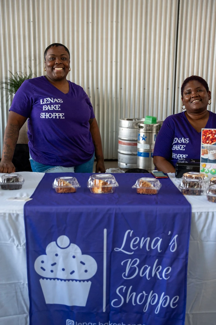 Two bakers standing behind a purple bake-shop table.
